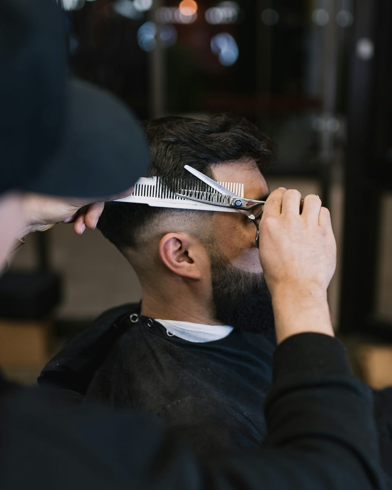 A barber cutting a client's hair with scissors in a barbershop