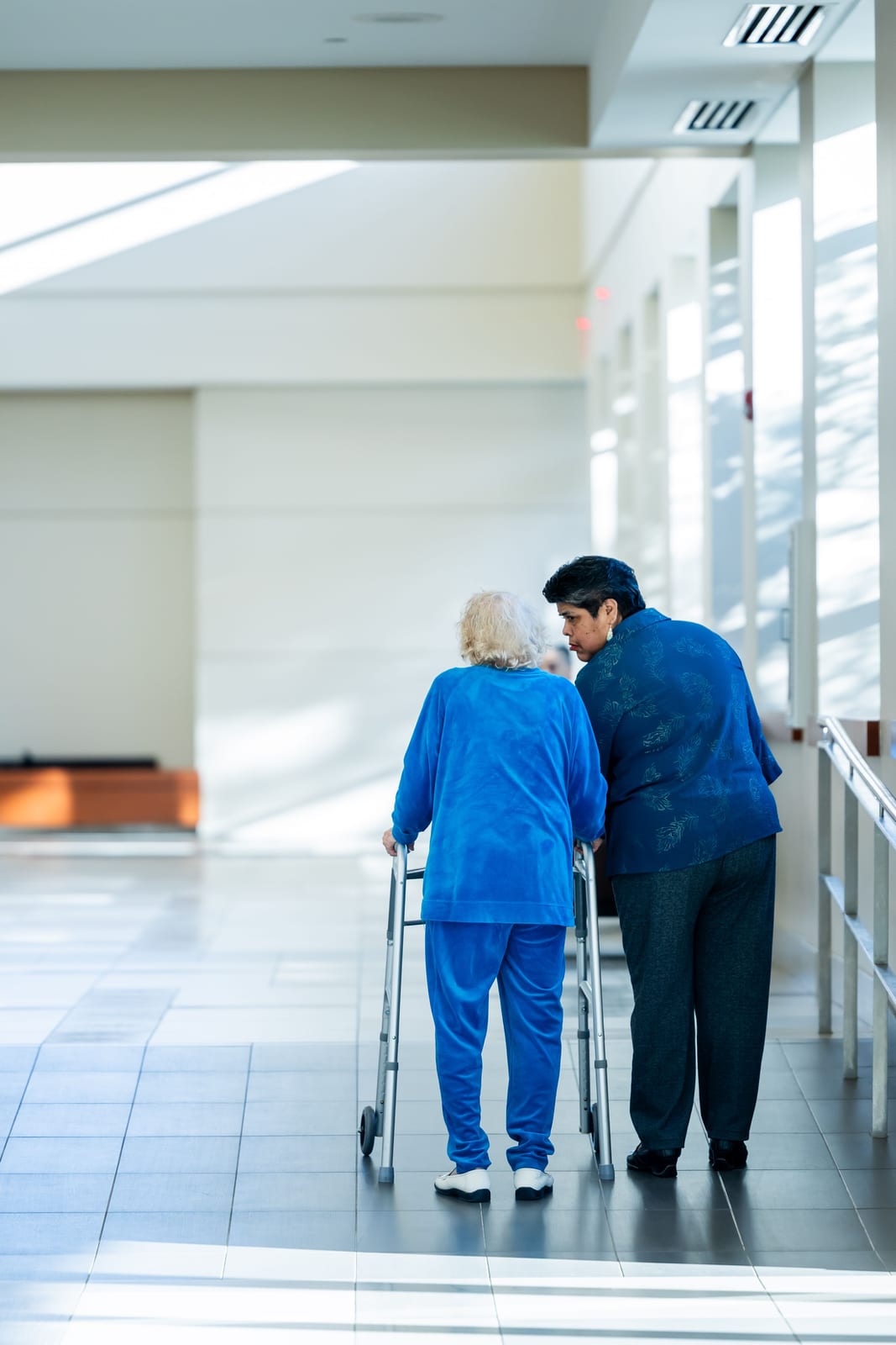 A nurse assisting an elderly patient with a walker in a hospital corridor