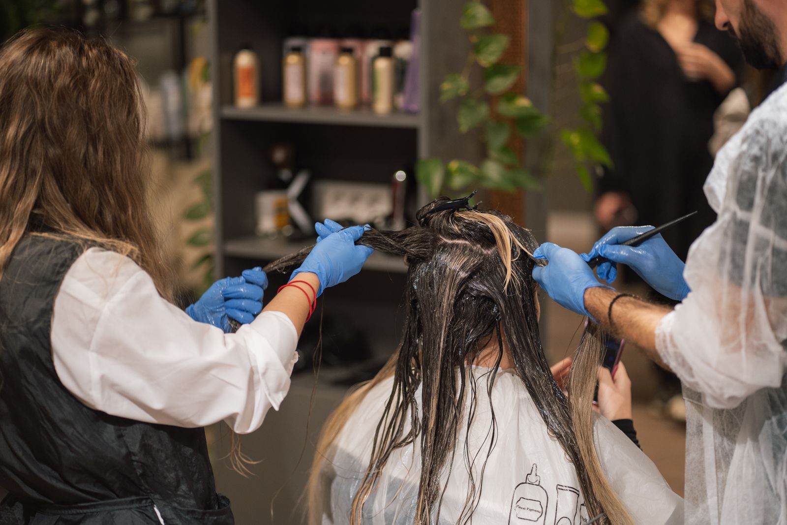 Two stylists applying chemical hair color to a client in a salon