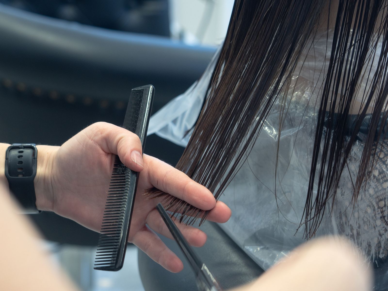 Close-up of a stylist cutting hair with scissors and a comb in a salon