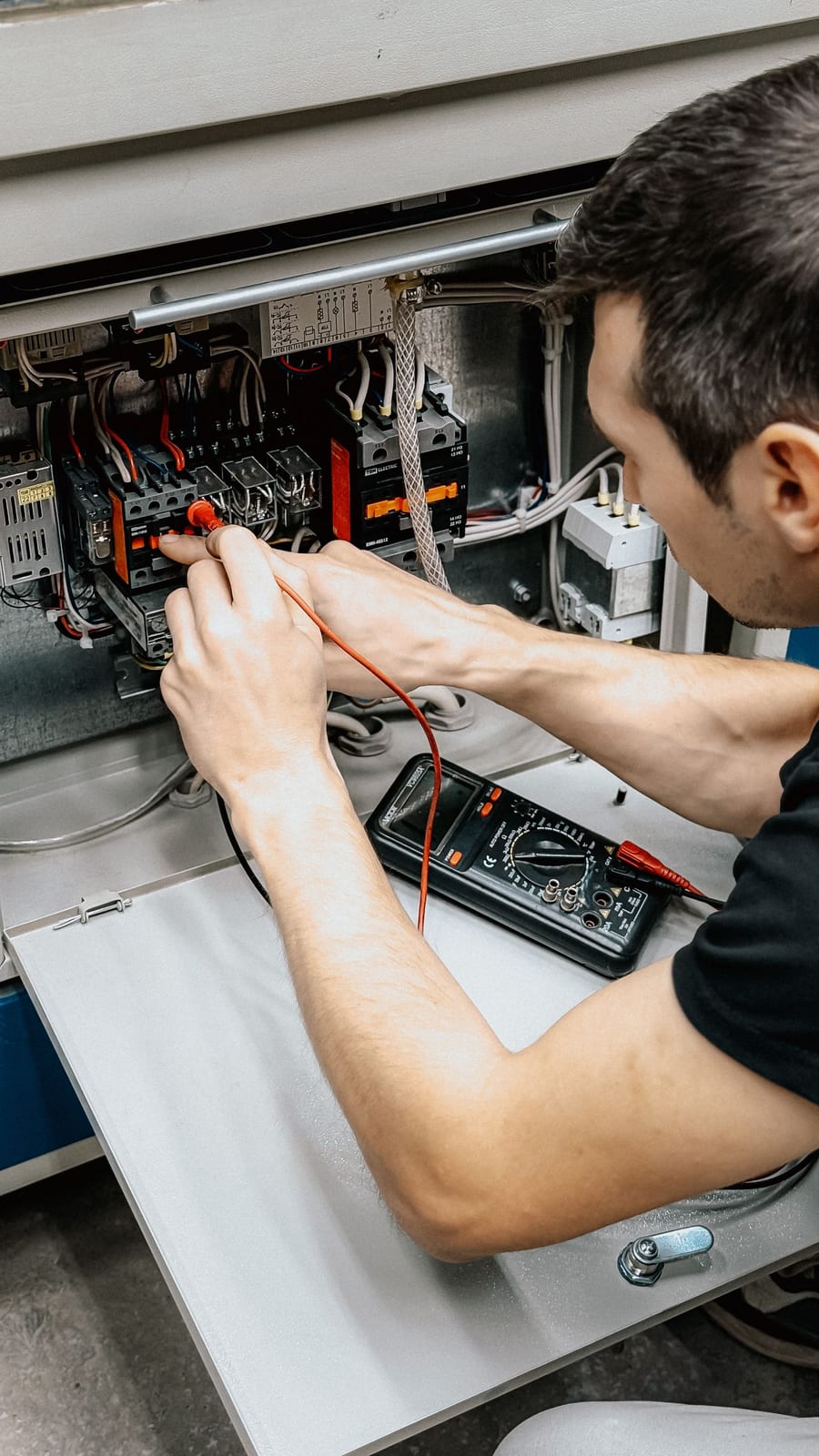 An electrician using a multimeter to diagnose connections inside an open electrical panel