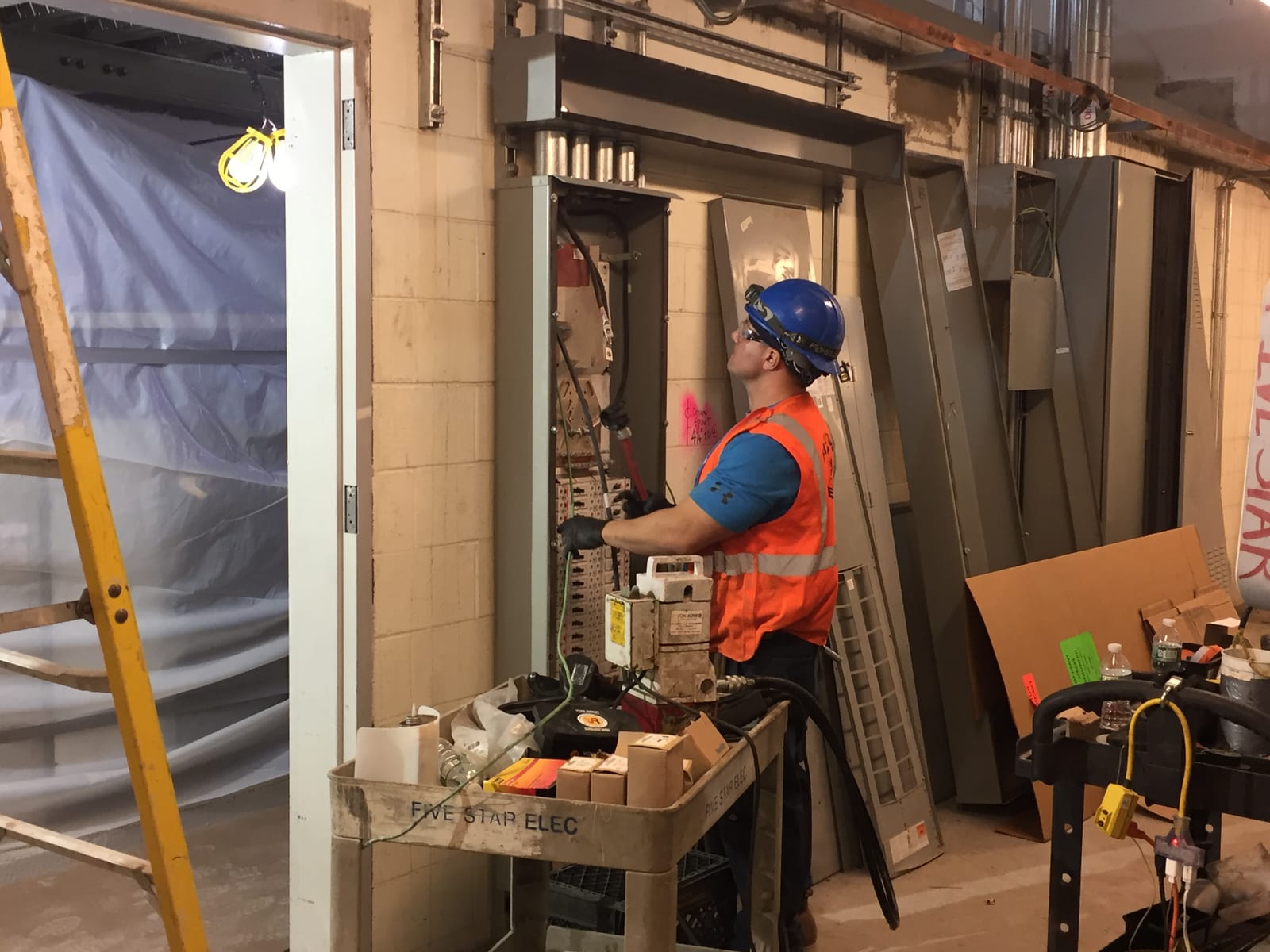An electrician pulling wires to an electrical panel in a substation room
