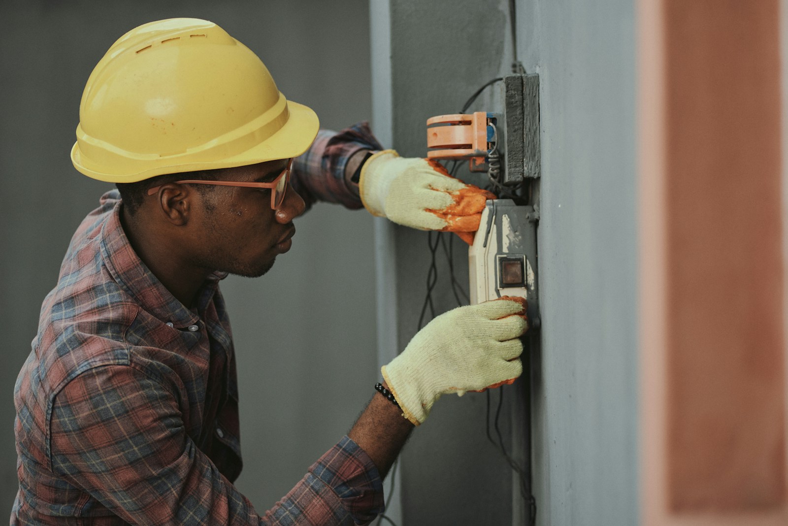 An electrician in a yellow hardhat and safety glasses installing wiring at a work site