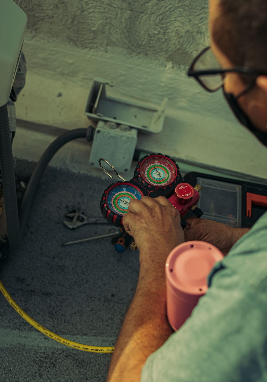 An HVAC technician working a refrigerant manifold gauge set during air conditioning maintenance