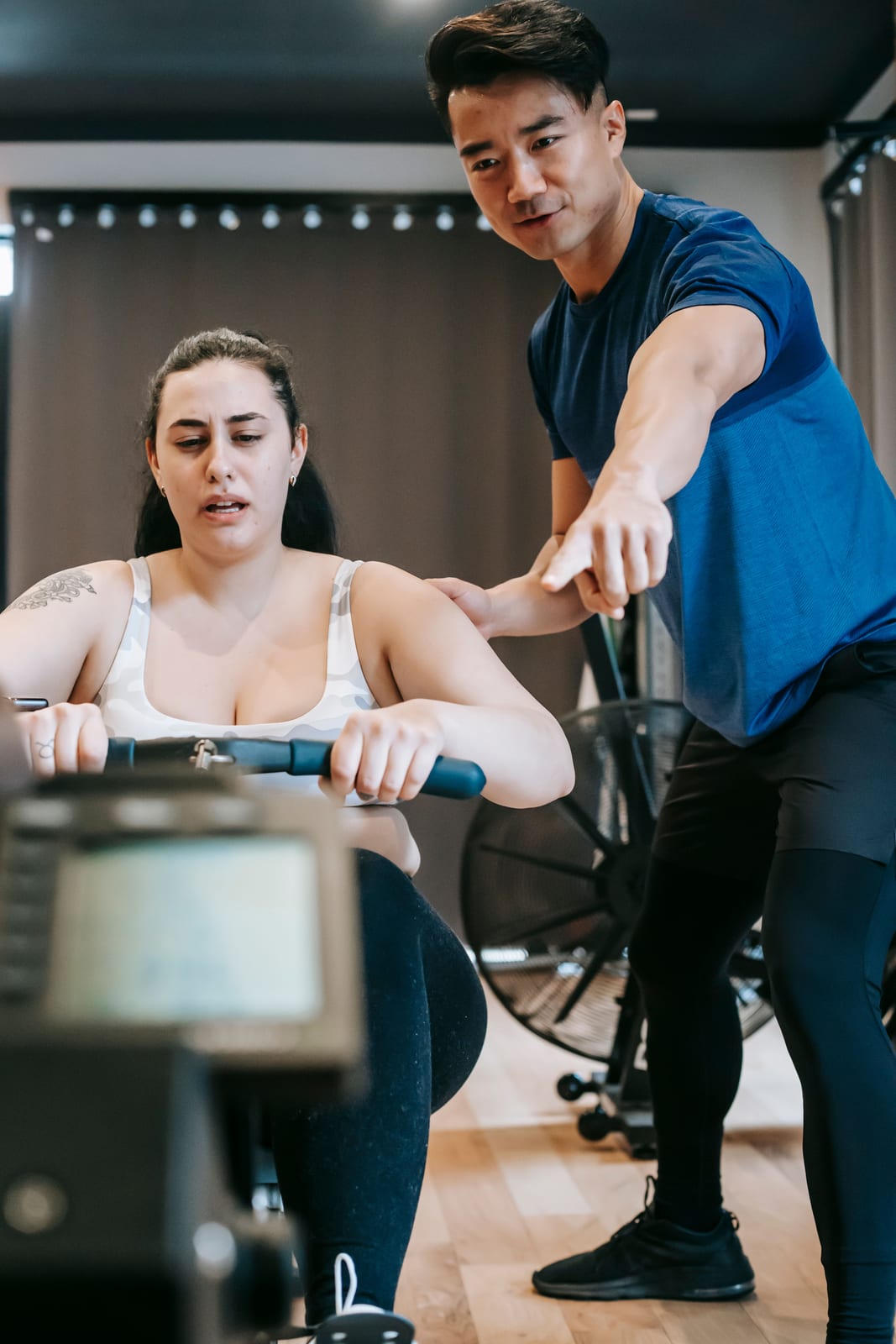 A personal trainer coaching a client through a rowing-machine exercise in a gym