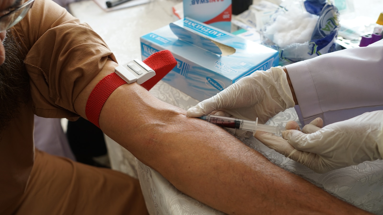 A phlebotomist drawing blood from a patient's arm with a tourniquet applied above the draw site