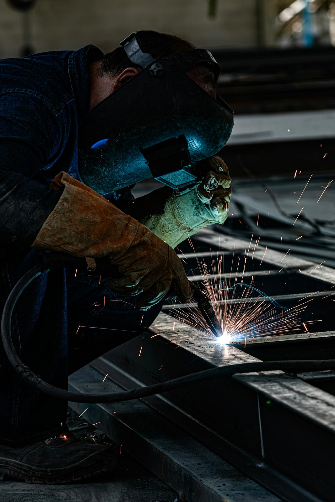 A welder mid-weld with the arc lit and sparks flying around the workpiece