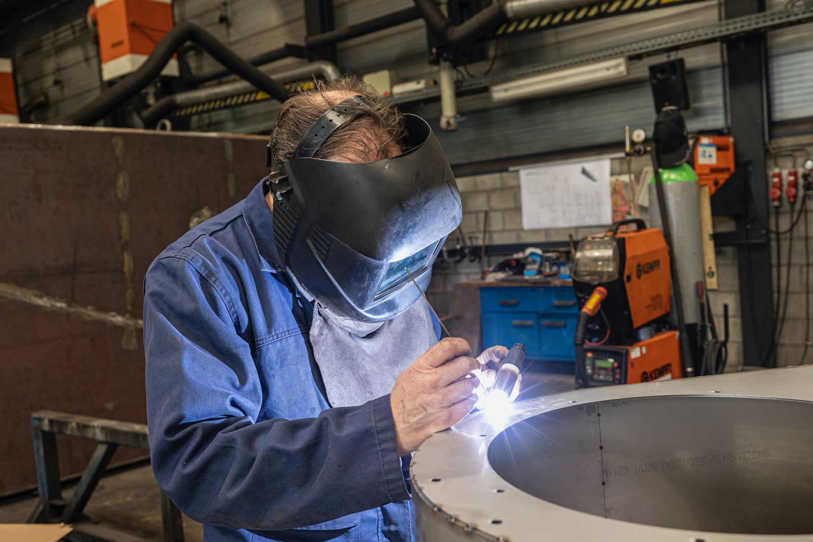 A welder in a modern shop working with the hood down on a circular metal flange