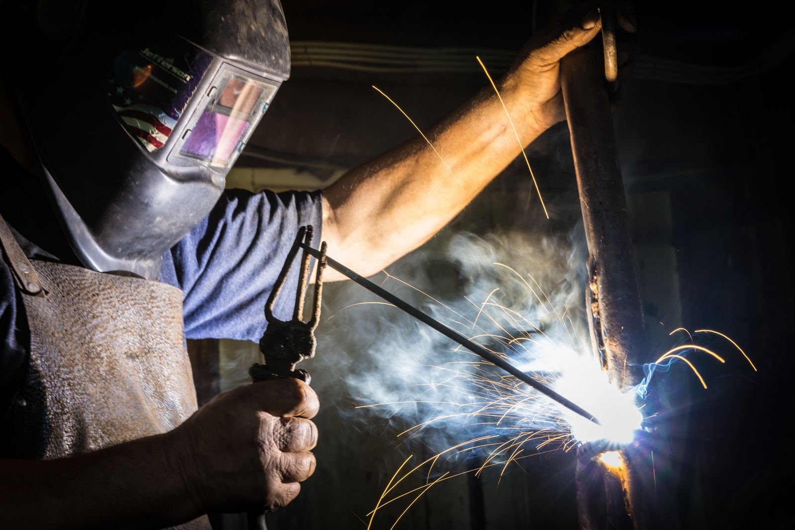 Close-up of a welder striking an arc, with gloves and a leather apron visible