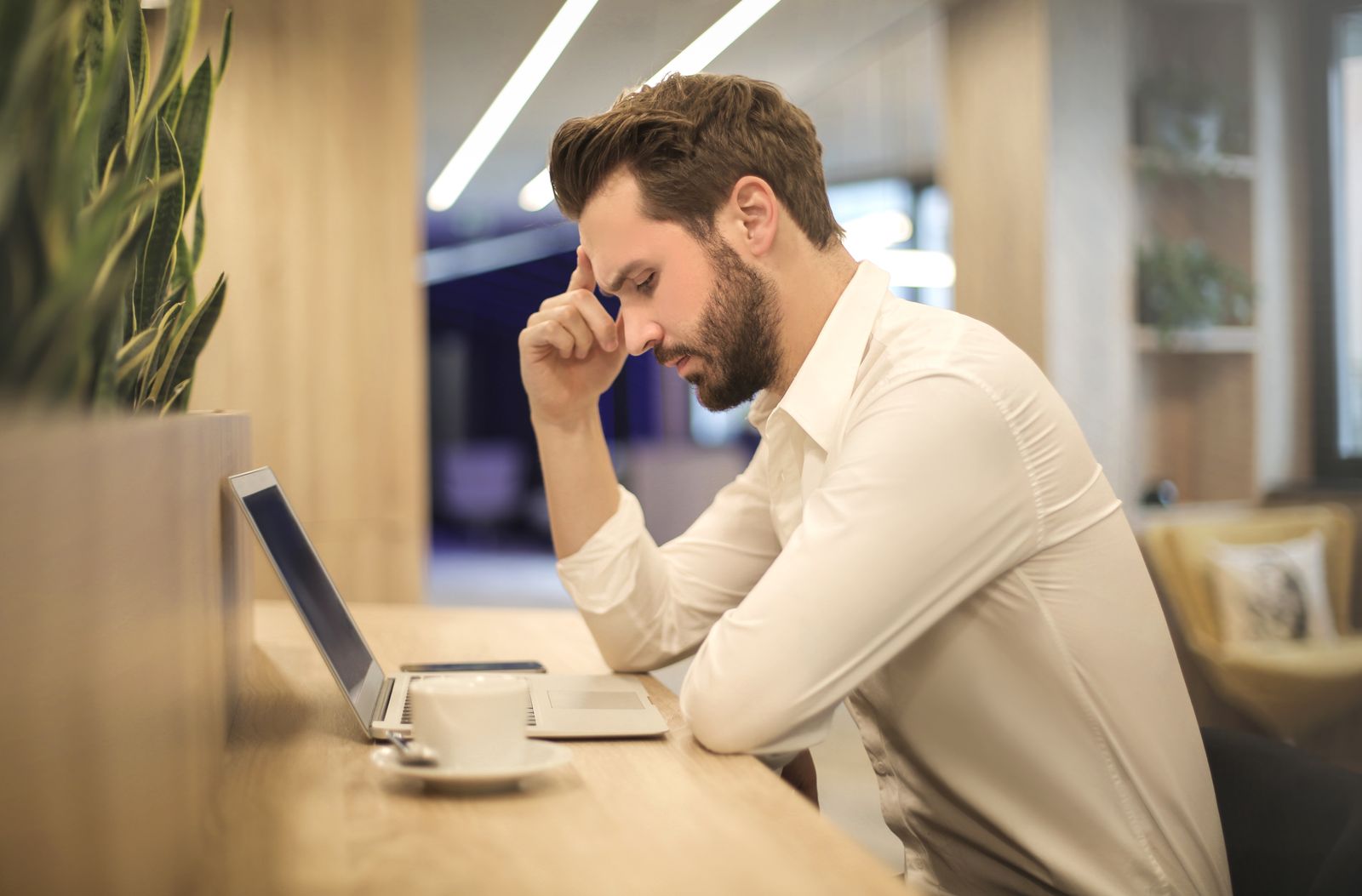 A person at a laptop with a hand to their forehead, weighing a decision.