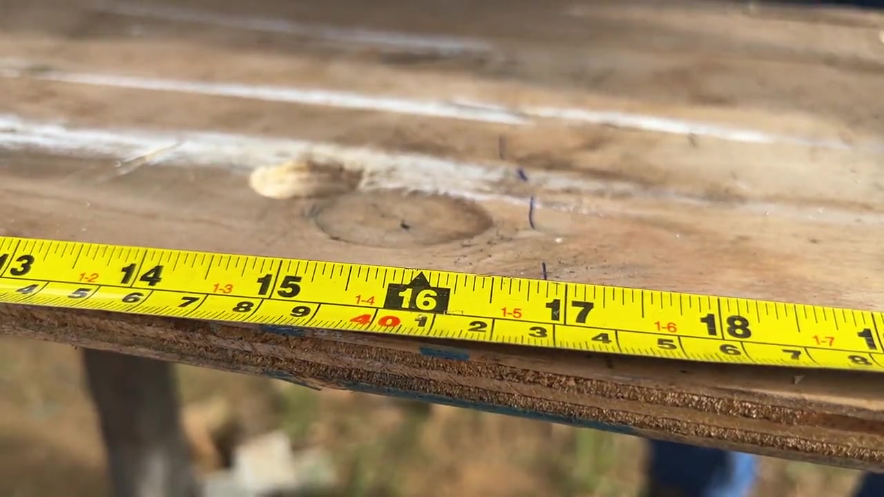 A tape measure held against a board, reading sixteen inches, as a cut line is marked.