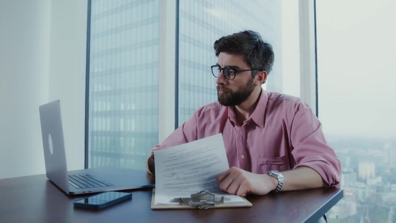 A printed document being read at a desk beside a laptop.